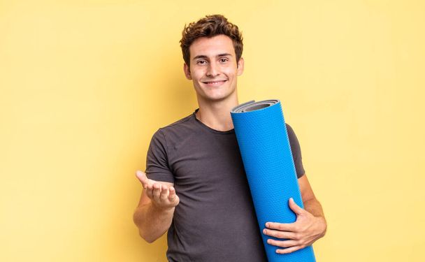 smiling happily with friendly, confident, positive look, offering and showing an object or concept. yoga mat concept - Фото, изображение