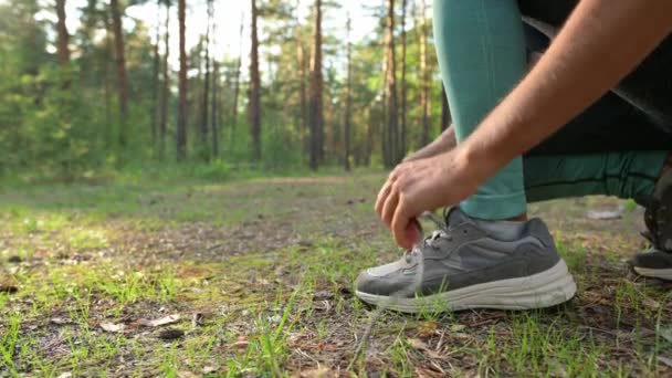 Çam ormanında koşmadan önce ayakkabı bağcıklarını bağlayan bir kız. - Video, Çekim
