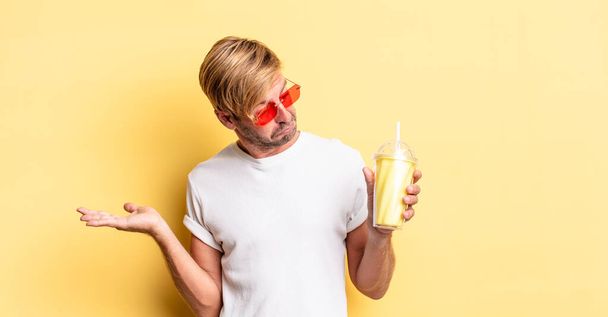 blond adult man feeling puzzled and confused and doubting with a milkshake - Fotó, kép
