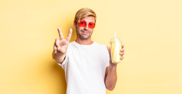blond adult man smiling and looking friendly, showing number two with a milkshake - Fotografie, Obrázek