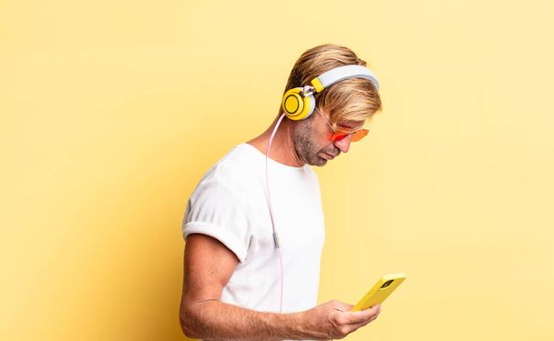 blond adult man on profile view thinking, imagining or daydreaming with headphones - Foto, Bild
