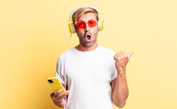 ξανθός ενήλικος άντρας που δείχνει έκπληκτος στη δυσπιστία με τα ακουστικά - Φωτογραφία, εικόνα