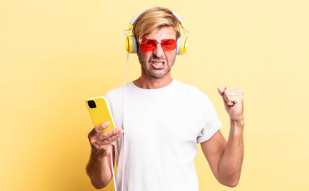 blond adult man shouting aggressively with an angry expression with headphones - Photo, image