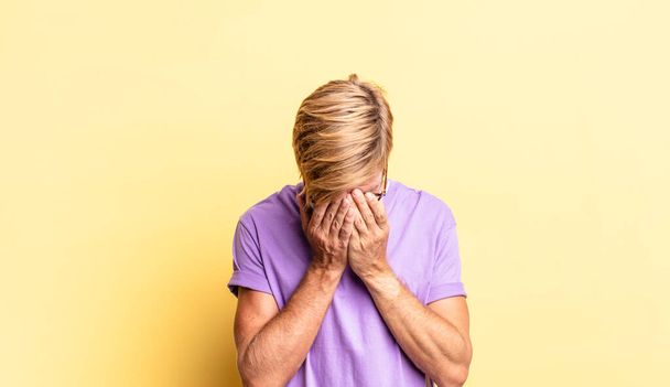 handsome blond adult man feeling sad, frustrated, nervous and depressed, covering face with both hands, crying - Фото, изображение