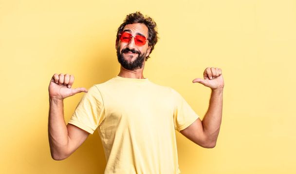 expressive crazy bearded man wearing sunglasses with a copy space against yellow wall - Фото, зображення