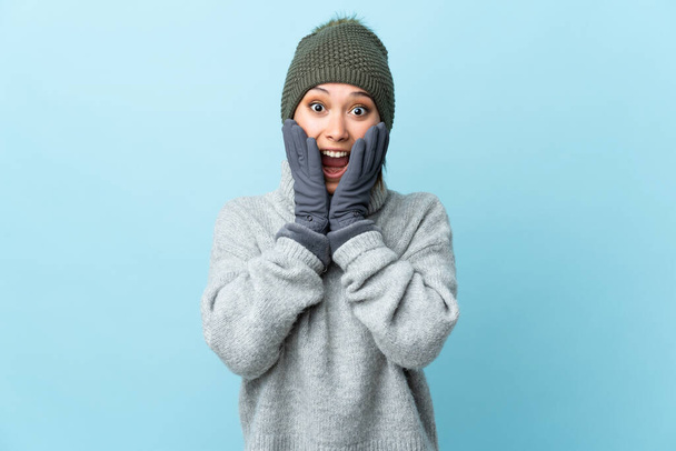 Young Uruguayan girl with winter hat isolated on blue background with surprise facial expression - Φωτογραφία, εικόνα