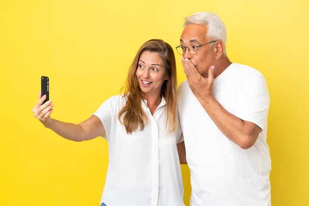 Coppia di mezza età isolata su sfondo giallo facendo un selfie con il cellulare - Foto, immagini
