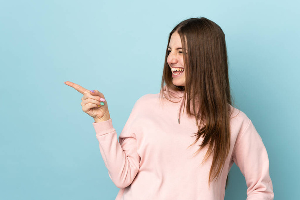 Молода біла жінка ізольована на синьому фоні, вказуючи пальцем на бік і представляючи продукт
 - Фото, зображення