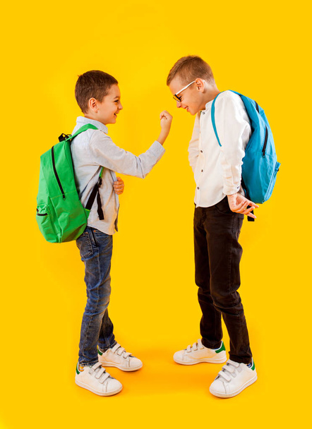 Cute schoolboys in uniform with backpacks on yellow background - Fotografie, Obrázek