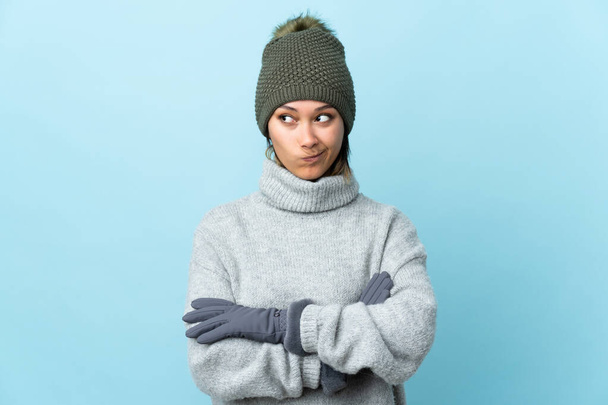 Young Uruguayan girl with winter hat isolated on blue background thinking an idea - Photo, Image