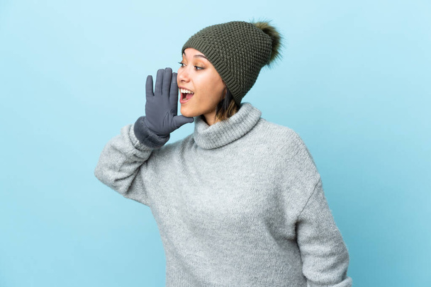 Giovane ragazza uruguaiana con cappello invernale isolato su sfondo blu urlando con la bocca spalancata - Foto, immagini