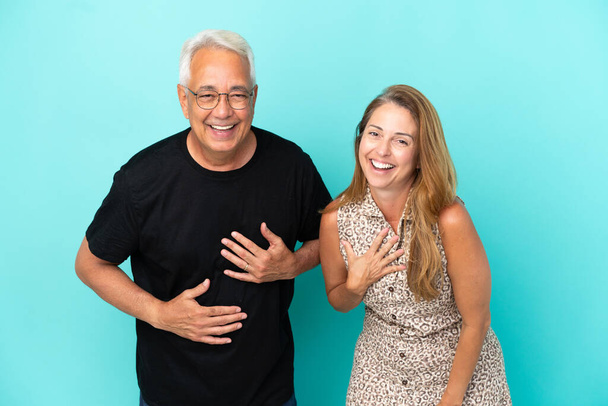 Keski-ikäinen pari eristetty sinisellä taustalla hymyillen paljon samalla kädet rinnassa - Valokuva, kuva