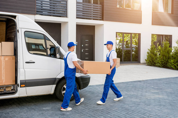 Two removal company workers unloading boxes from minibus into new home - Fotografie, Obrázek