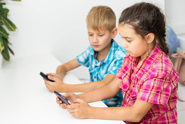Junge spielt mit Smartphone neben seiner Schwester im heimischen Zimmer. - Foto, Bild
