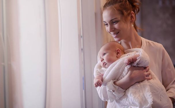 Mom with a newborn baby in her arms. The girl is holding a baby in front of the window. Newborn on mother hands - Фото, зображення