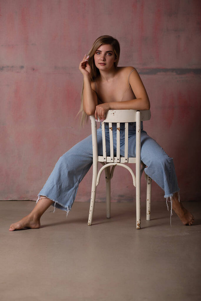 Sexy fashionable blonde posing in a bra and jeans. A girl with a perfect slender body. A studio photo. - Foto, Imagen