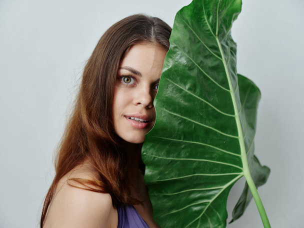 pretty woman covers her face with green leaf exotic isolated background - Photo, Image