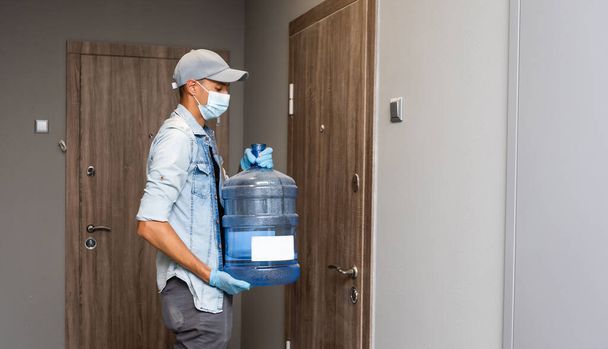 Livraison de l'eau homme porter masque médical protecteur visage pendant la pandémie de coronavirus - Photo, image