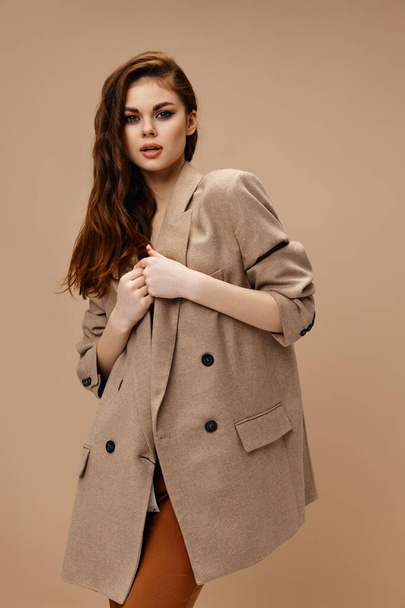 fashionable woman in a coat and keychains gesturing with her hands on a beige background - Foto, immagini