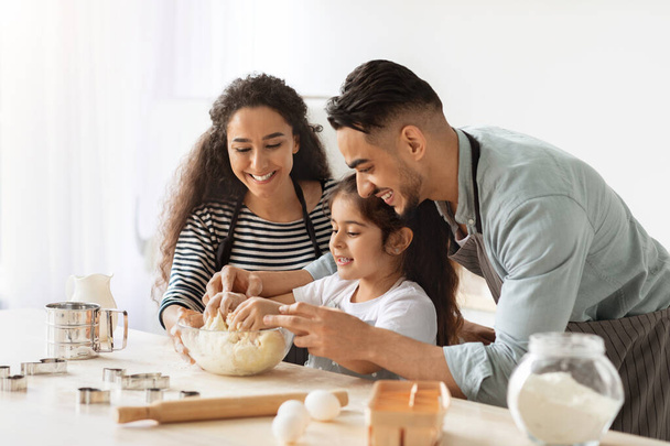 Vrolijke vader, moeder en dochter bakken samen thuis - Foto, afbeelding