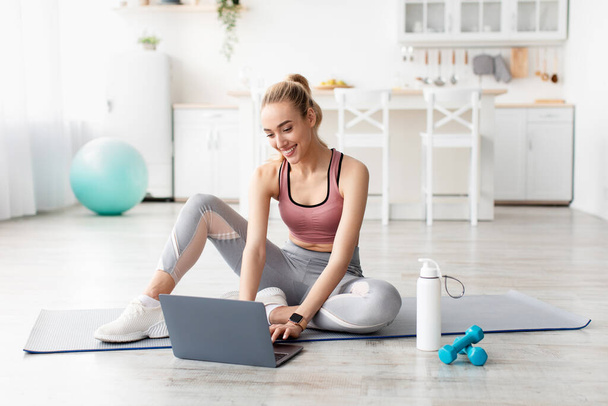 Sonriente caucásica linda joven rubia fitness blogger mujer mirando el ordenador portátil, charlando y eligiendo lección de entrenamiento en línea - Foto, imagen