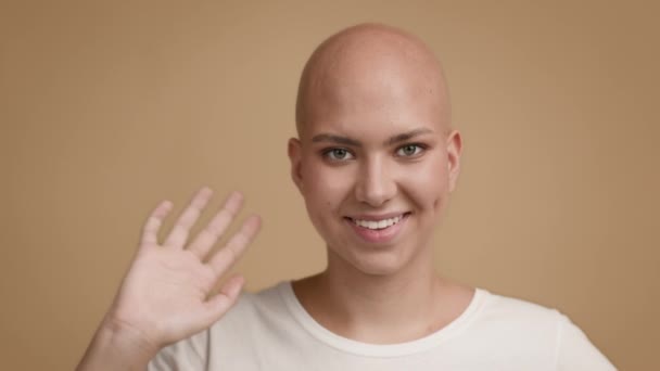 Hairless giovane donna che saluta mano sorridente in posa su sfondo beige - Filmati, video