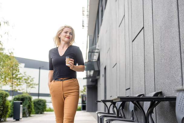 χαρούμενα μοντέρνο ξανθιά κρατώντας καφέ σε εξωτερικούς χώρους - Φωτογραφία, εικόνα