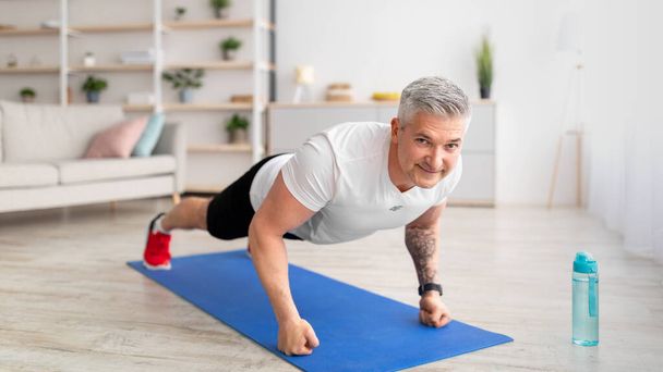 Happy sportowy Dojrzały mężczyzna robi push-up ćwiczenia na pięści, ćwiczy w domu w salonie wnętrza - Zdjęcie, obraz