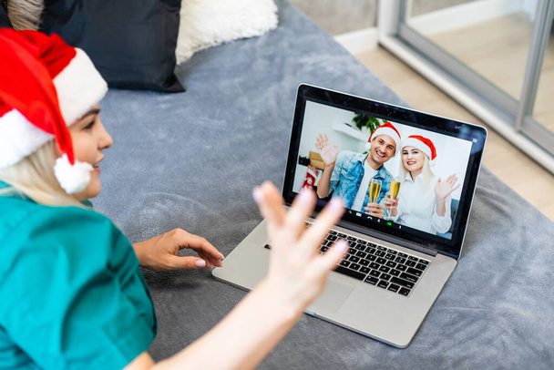Lächelndes Mädchen mit Weihnachtsmütze, das per Webcam die Familie anruft. Frau mit Laptop sitzt zu Hause in der Küche im virtuellen Meeting-Chat im Urlaub. Frohe Weihnachten und Neues Jahr neue Normalität. - Foto, Bild