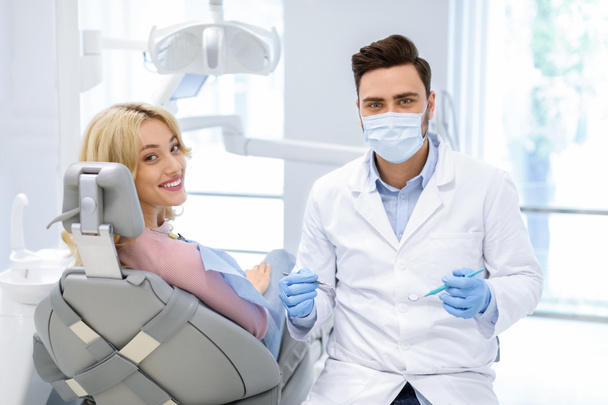 A páciens és férfi orvos fogászati eszközökkel a kamerába néz - Fotó, kép