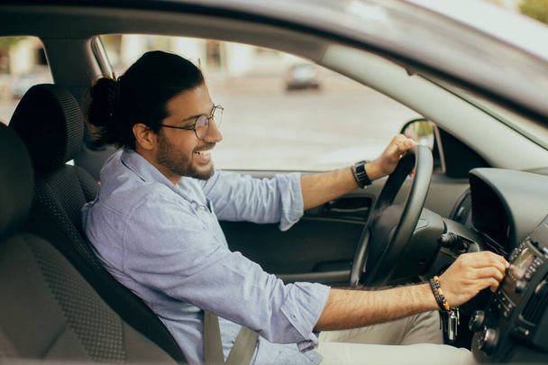 Cheerful arab guy with fasten seat belt turning on music - Photo, Image