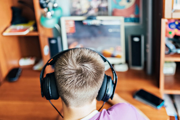 10代の男の子、コンピュータでビデオゲームをしている若い男、技術を使って、ヘッドフォンを着て、コンピュータを使っています。彼はビデオゲームをする。ヘッドフォンの使用 - 写真・画像