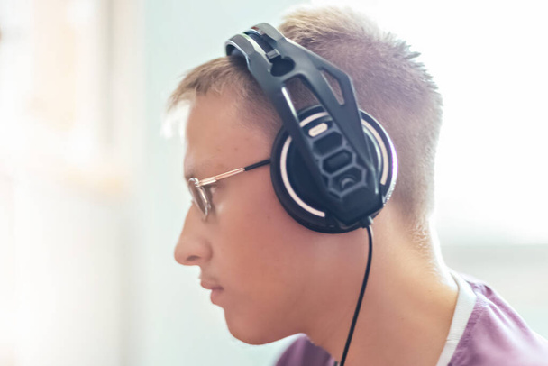 Ein Junge im Teenageralter, ein junger Mann, der Videospiele auf einem Computer spielt, Technologie benutzt, Kopfhörer trägt, einen Computer benutzt. Ein junger Mann, ein Teenager, der Technologie benutzt. - Foto, Bild
