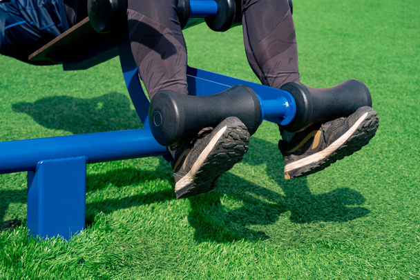 piernas de una persona, la realización de ejercicios abdominales utilizando una máquina de ejercicio al aire libre sit-up banco - Foto, imagen
