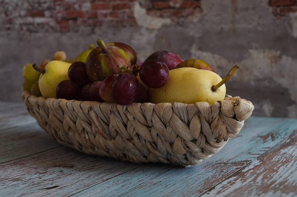 Nature morte aux fruits poires et prunes reposent sur une assiette en osier en forme de bateau qui se dresse sur des planches dans le style provençal contre le mur - Photo, image