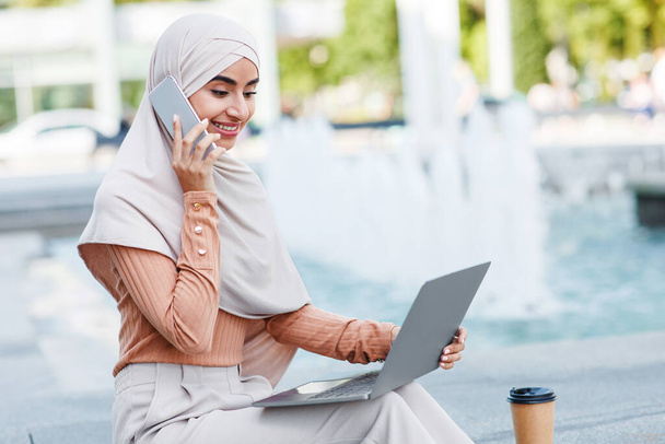 Happy millennial arab islamic female in hijab digital nomad calls on smartphone - Photo, Image