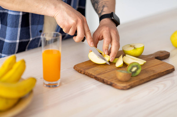 Неузнаваемый зрелый мужчина режет фрукты для смузи или свежего сока, готовит еду за кухонным столом - Фото, изображение