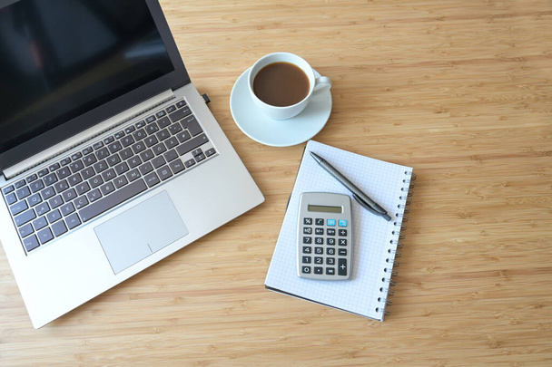 Laptop computer, calculator, spiral book and coffee, flat lay on a wooden desk, business accounting concept, view from above, copy space, selected focus - Photo, image