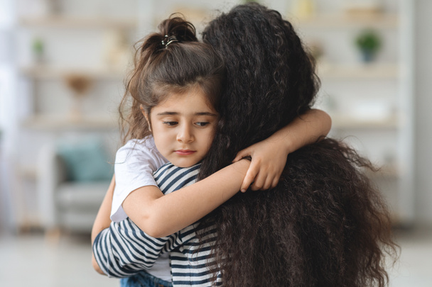 Расстроенная маленькая девочка обнимает свою маму, крупным планом портрет - Фото, изображение