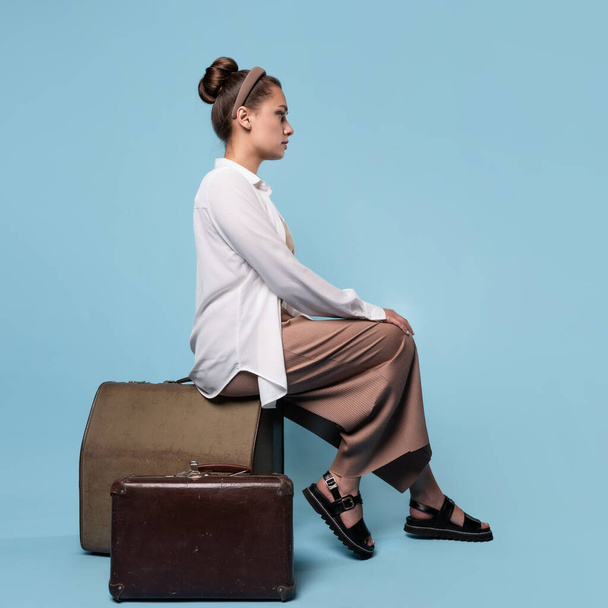 young woman in summer pants and a white shirt is sitting on vintage leather suitcases - Foto, Imagem