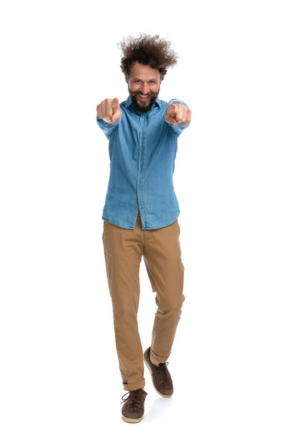 ευτυχής casual άνθρωπος με τα πόδια προς την κάμερα και δείχνει με τα δύο χέρια σε λευκό φόντο - Φωτογραφία, εικόνα
