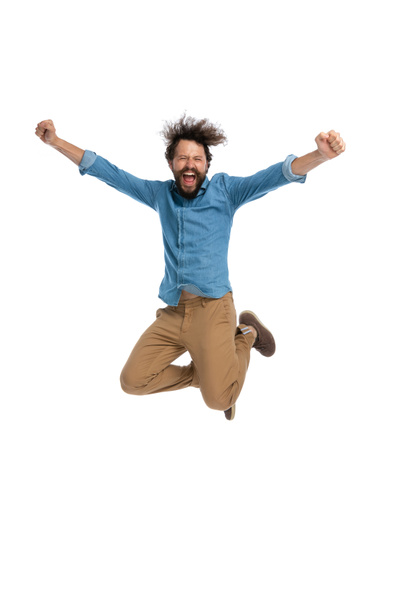 pohledný ležérní muž skákání do vzduchu a slaví úspěch na bílém pozadí - Fotografie, Obrázek