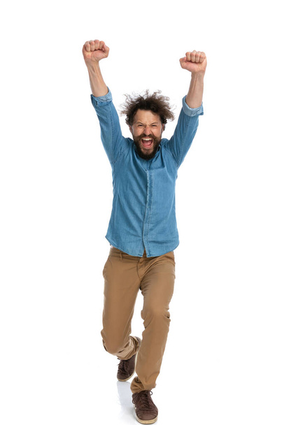 podekscytowany swobodny mężczyzna idzie w kierunku kamery i świętuje zwycięstwo na białym tle - Zdjęcie, obraz