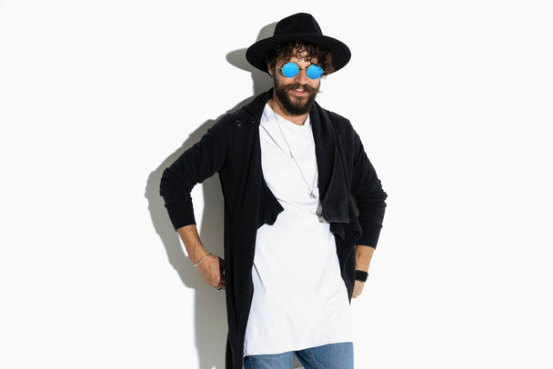 young hipster holding his hands behind him, smiling and wearing a black cardigan on white background - Photo, Image
