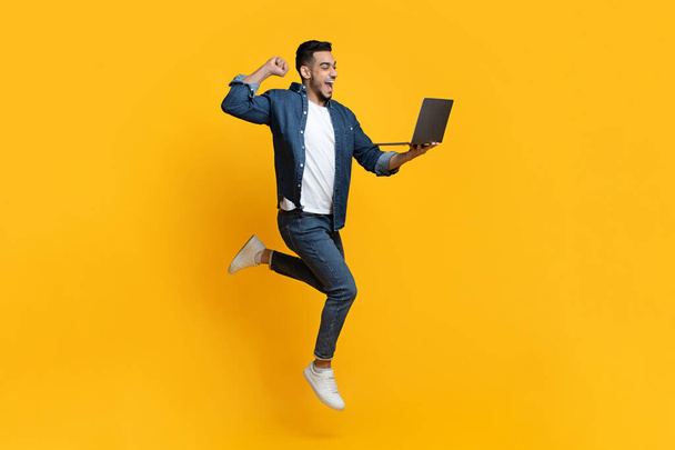 Emocjonalny arabski facet przy użyciu nowego nowoczesnego laptopa na żółty - Zdjęcie, obraz