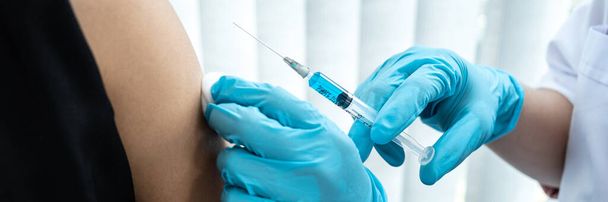 Doctor in medical glove holding syringe to injection coronavirus vaccine in the shoulder of patient to protection from covid-19 pandemic during doctor made an appointment at hospital - Foto, Bild