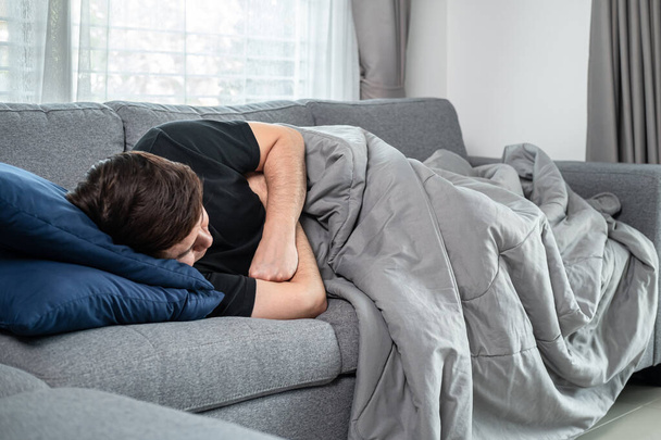 Asian man is lying with blanket on couch at home to rest when feeling sick from high fever, migraine and headache - Foto, Imagem