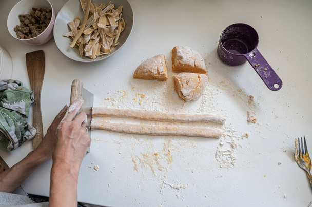 Draufsicht einer Frau, die köstliche frische italienische Gnocchi auf einer mit Mehl bestäubten Küchentheke zubereitet. - Foto, Bild