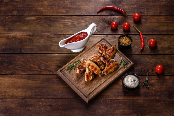 Grilled spicy chicken wings on a dark background with spices and herbs. Unhealthy food cooked on fire - Photo, Image