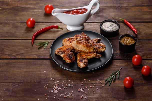 Grilled spicy chicken wings on a dark background with spices and herbs. Unhealthy food cooked on fire - Photo, image